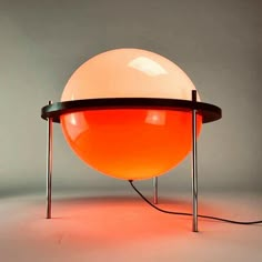 an orange ball lamp sitting on top of a metal stand next to a gray wall