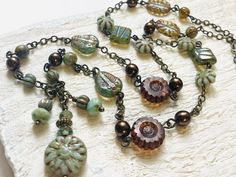 Pretty verdigris green Czech glass beads and bronzy pearls dot this boho chic Y pendant necklace.  Stylized flower and leaf beads, melon beads and more can all be found here linked together on antiqued brass chain.  Lightweight and pretty - perfect compliment for dresses and tops and great for layering too! * Measures 24 inches long * Ready to Ship! * Gift Wrap Upgrade is available on this item  * Eligible for Etsy's Free Shipping Guarantee Back to StoneandFiber's Home Page: https://www.etsy.com Flower Bead Necklace, Czech Beads Jewelry, Pewter Ring, Czech Glass Necklace, Czech Glass Jewelry, Leaf Beads, Handmade Pendant Necklace, Magical Jewelry, Y Necklace