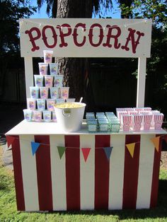 an outdoor popcorn stand is set up with cupcakes and cups on the table