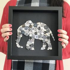 a woman holding up a framed button art piece with an elephant made out of buttons