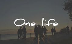 a group of people standing on top of a beach next to the ocean at sunset