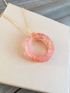 a pink necklace with a gold chain hanging from it's center on top of a piece of paper