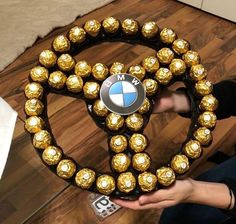 a person holding up a gold and black bmw belt with chocolate balls on it's side