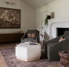 a living room with two chairs and a ottoman in front of a fire place on the wall