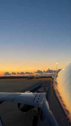 an airplane is sitting on the tarmac at sunset with clouds in the sky behind it