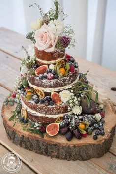 a three tiered cake with fresh fruit and flowers on top is sitting on a wooden table