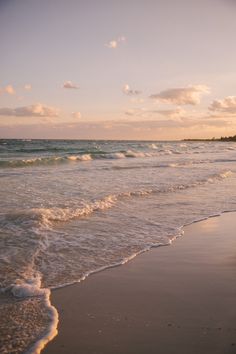 a person walking along the beach with their surfboard in hand and waves crashing on the shore