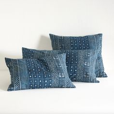 two blue pillows sitting on top of a bed next to each other in front of a white wall