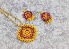 two pieces of jewelry sitting on top of a white cloth covered table next to a gold necklace and earring