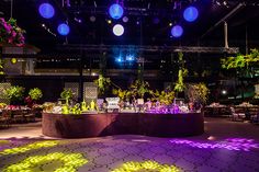 an indoor event with purple and green lights on the ceiling, decorated with flowers and greenery