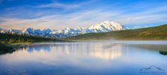 a lake surrounded by mountains and trees in the foreground with blue sky above it