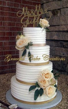 a three tiered cake with white flowers and gold trimmings on a table