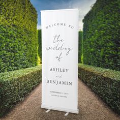 a welcome sign for the wedding of ashley and benjamin in front of topiary hedges