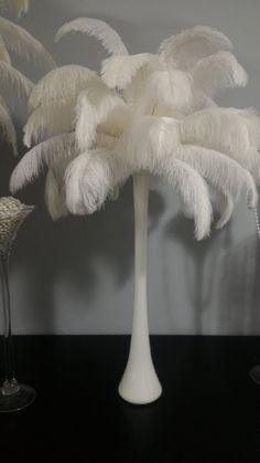 a tall white vase filled with feathers on top of a black table next to two wine glasses