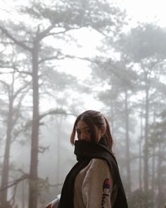 a woman standing in the woods wearing a scarf