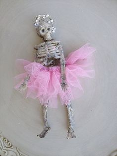 a skeleton in a pink tutu is sitting on a white plate with silver trim