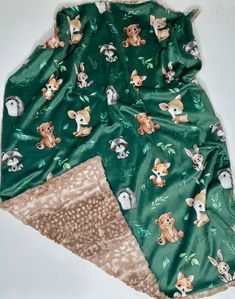 the green blanket has animals on it and is next to a brown teddy bear pillow