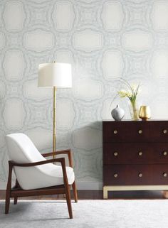 a white chair sitting in front of a wooden dresser next to a lamp on top of a table