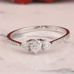 three stone heart shaped diamond ring with red band on marble countertop next to rose