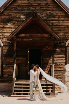 a bride and groom standing in front of a wooden building with their veil blowing in the wind