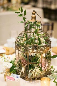 a birdcage filled with flowers and greenery on top of a white table