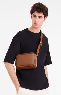 a man in black shirt and white pants holding a brown leather shoulder bag on his chest