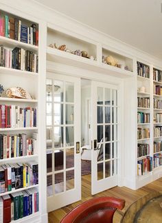 a living room filled with lots of books on top of white book shelves next to a red chair