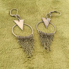 These fun geometric charm earrings come in a subtle antique brass finish. Each earring has a cascade of dainty chains hanging from a hoop in a chainmail reminiscent pattern. These bold and lively earrings are sure to make an impression. With a matching necklace available, this would make a fabulous gift set! -Geometric triangle and hoop charm -hanging chain accents -Antique brass finish -Leverback earring closure Bohemian Geometric Nickel-free Jewelry, Nickel-free Geometric Brass Earrings, Vintage Brass Dangle Hoop Earrings, Bronze Nickel-free Chandelier Earrings In Brass, Bohemian Geometric Metal Jewelry, Bronze Nickel-free Brass Chandelier Earrings, Bohemian Triangle Nickel-free Earrings, Nickel-free Bronze Dangle Hoop Earrings, Handmade Geometric Brass Jewelry