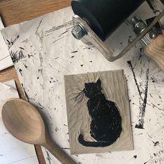 a black cat is sitting on a piece of paper next to a wooden spoon and knife