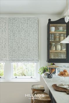 Abstract line print Roman blinds in a monochrome kitchen with open glass cabinets, a marble worktop and pastries on the counter. Monochromatic Colour Scheme, Abstract Line Pattern, Monochromatic Colour, Line Print, Monochromatic Color Scheme, Line Pattern, Line Patterns