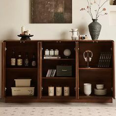 a wooden cabinet filled with lots of books and vases next to a wall mounted painting