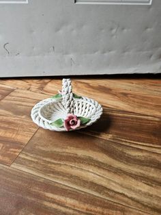 a white basket sitting on top of a hard wood floor next to a door with a pink flower in it