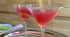 two wine glasses filled with pink liquid on a silver tray next to plates and utensils