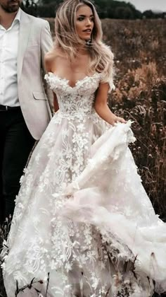 a man and woman are walking through the grass together, dressed in wedding gowns