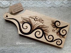 a wooden cutting board with an intricate design on the front and back side, sitting on a lace - covered tablecloth