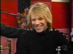 a man smiling while sitting in front of a microphone and recording equipment on the television set