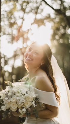 a woman in a wedding dress is smiling and holding a bouquet with white flowers on it