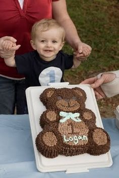 a baby standing in front of a teddy bear cake