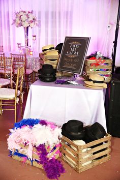 a table topped with lots of hats next to a white table cloth covered wall and purple drapes