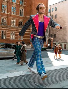 a man in plaid pants is dancing on the sidewalk with other people walking around him