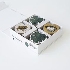 four coasters in a box on a white surface with an animal and plant motif