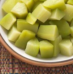 a white bowl filled with cut up pieces of green food on top of a woven table cloth