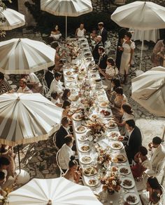 an overhead view of a long table with umbrellas and people sitting at tables eating