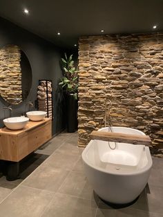 a bathroom with stone walls and two sinks in the center, along with a large round mirror on the wall