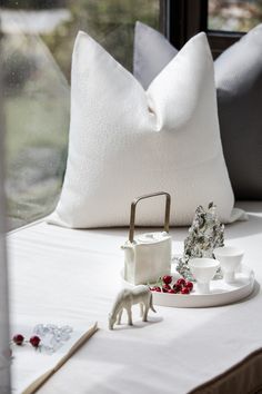 a white table topped with pillows and figurines on top of a bed next to a window