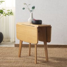 a small wooden table with a vase on top and two plants sitting on it's side