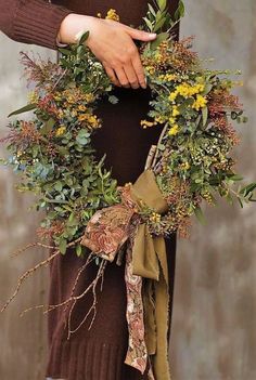 a woman wearing a brown sweater holding a wreath with yellow flowers and green leaves on it