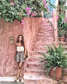 a woman standing in front of some steps with pink flowers growing on the wall behind her