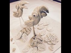 two ceramic figurines sitting on top of a white table covered in leaves and flowers