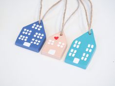 three small wooden houses are hanging from twine strings on a white surface with a red heart in the center